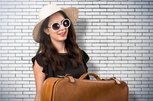 Красивая молодая девушка с чемоданом на кирпичной стене — стоковое фото