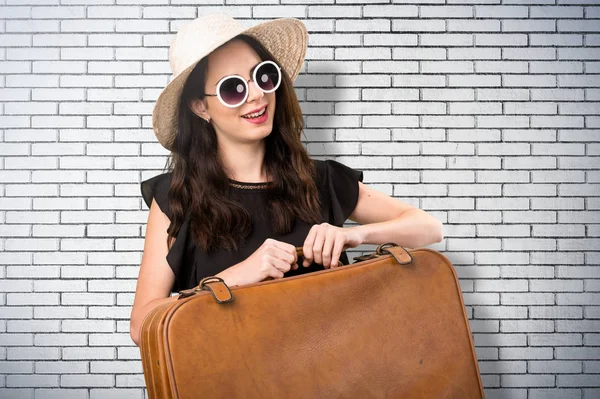 Menina bonita com uma mala em uma parede de tijolo — Fotografia de Stock