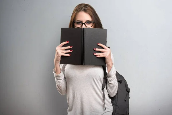 Studentin versteckt sich hinter einem Buch auf strukturiertem Hintergrund — Stockfoto