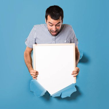 Bir kağıt ile boş bir afiş tutarak şaşırmış yakışıklı adam 