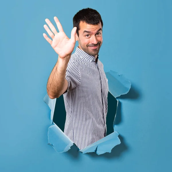 Hombre guapo saludando a través de un agujero de papel — Foto de Stock