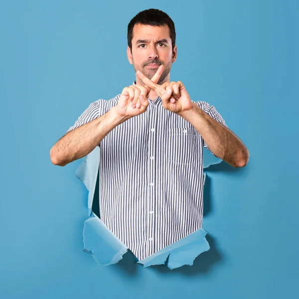 Hombre guapo haciendo ningún gesto a través de un agujero de papel — Foto de Stock