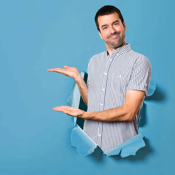 Hombre guapo presentando algo a través de un agujero de papel — Foto de Stock