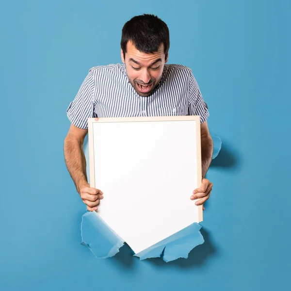 Surpreendido Bonito homem segurando um cartaz vazio através de um papel — Fotografia de Stock
