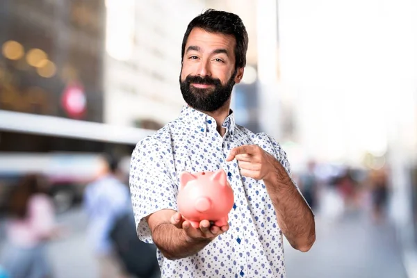 Handsome brunette man with beard holding a piggybank — Stock Photo, Image