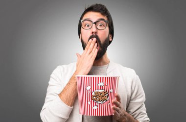 Sürpriz Hipster adam yeme popcorns gri arka plan üzerinde