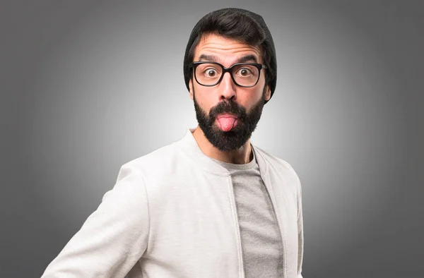 Hipster uomo tirando fuori la lingua su sfondo grigio — Foto Stock