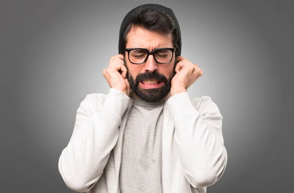 Hipster hombre cubriendo sus oídos sobre fondo gris —  Fotos de Stock