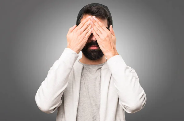 Hipster man die betrekking hebben op zijn ogen op grijze achtergrond — Stockfoto