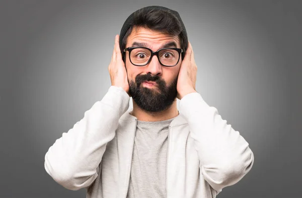 Hipster-Mann verhüllt seine Ohren vor grauem Hintergrund — Stockfoto