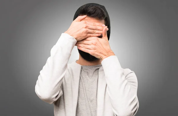 Hipster man die betrekking hebben op zijn gezicht op grijze achtergrond — Stockfoto