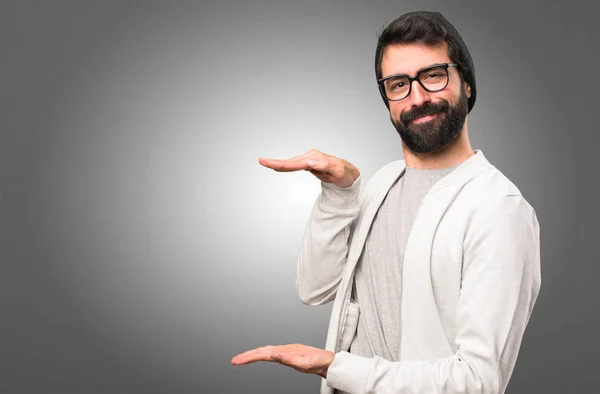 Hipster hombre sosteniendo algo sobre fondo gris — Foto de Stock