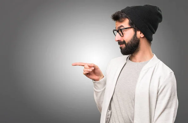 Hipster man pointing to the lateral on grey background — Stock Photo, Image