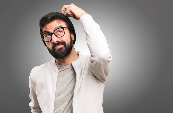 Hipster man having doubts on grey background — Stock Photo, Image