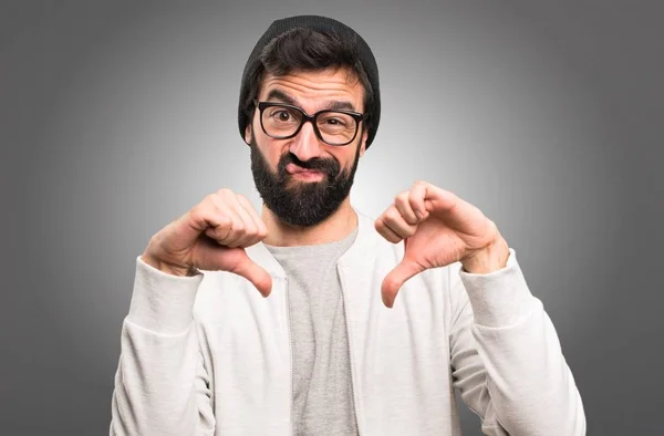 Hipster hombre haciendo mala señal sobre fondo gris — Foto de Stock