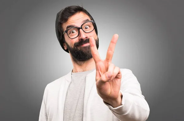 Hipster man making victory gesture on grey background — Stock Photo, Image