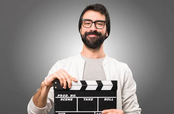 Happy Hipster man holding a clapperboard on grey background — Stock Photo, Image