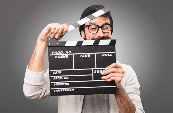 Hipster man holding a clapperboard on grey background — Stock Photo, Image