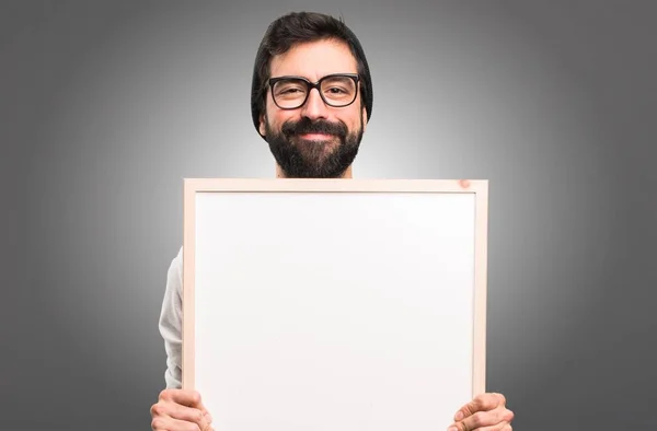 Feliz Hipster homem segurando um cartaz vazio no fundo cinza — Fotografia de Stock