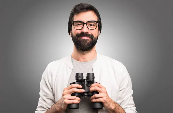 Feliz Hipster homem com binóculos em fundo cinza — Fotografia de Stock