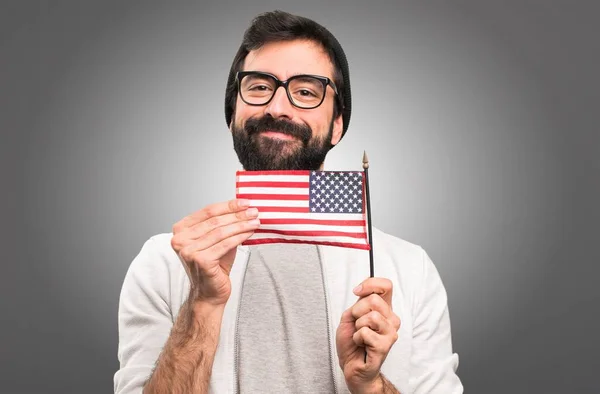 灰色の背景にアメリカの国旗を保持している流行に敏感な男 — ストック写真