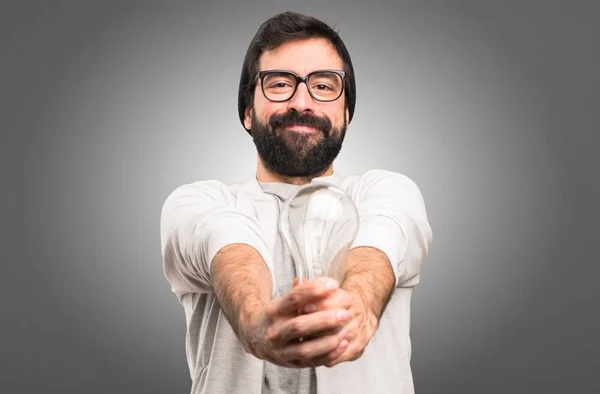 Feliz hombre Hipster sosteniendo una bombilla sobre fondo gris —  Fotos de Stock