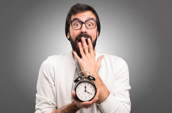 Surprised Hipster man holding vintage clock on grey background