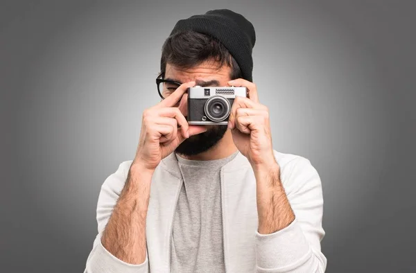 Hipster man holding a camera on grey background — Stock Photo, Image