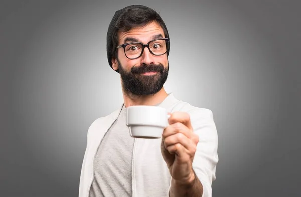 Feliz Hipster homem segurando uma xícara de café no fundo cinza — Fotografia de Stock