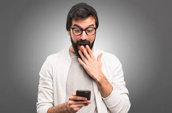 Překvapený muž Hipster mluvit mobilní na šedém pozadí — Stock fotografie