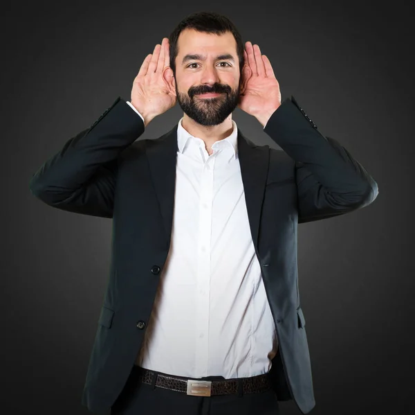 Bonito homem de negócios ouvindo algo no fundo preto — Fotografia de Stock