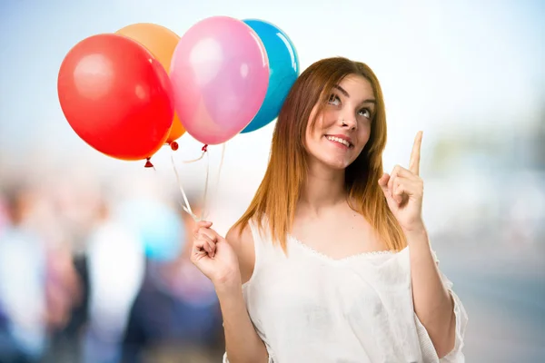 Menina bonita segurando um balão e apontando para cima em unfocu — Fotografia de Stock