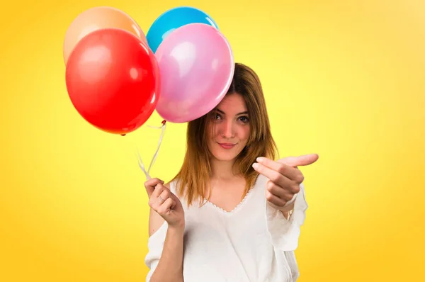 Beautiful young girl holding a balloon and doing coming gesture — Stock Photo, Image