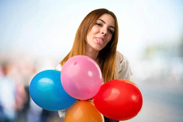 Hermosa joven sosteniendo un globo y sacando su lengua — Foto de Stock