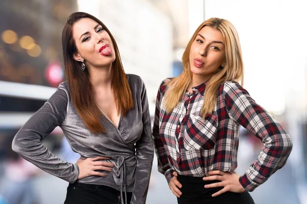 Two friends taking out their tongue on unfocused background — Stock Photo, Image