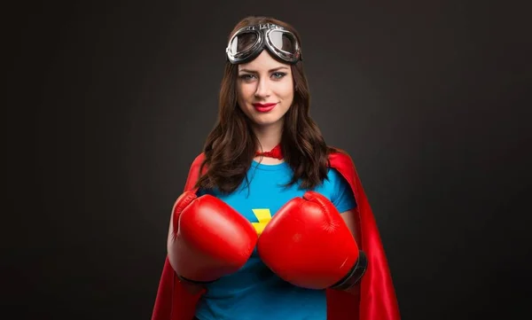 Menina super-herói bonita com luvas de boxe no fundo preto — Fotografia de Stock
