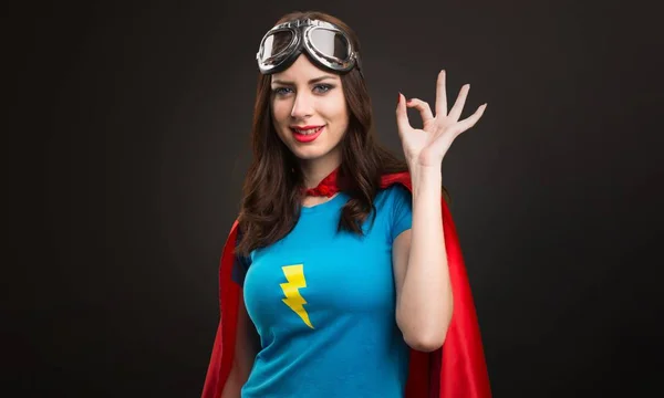 Bastante chica superhéroe haciendo OK signo sobre fondo negro — Foto de Stock