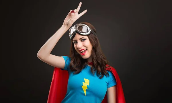 Pretty superhero girl making victory gesture on black background