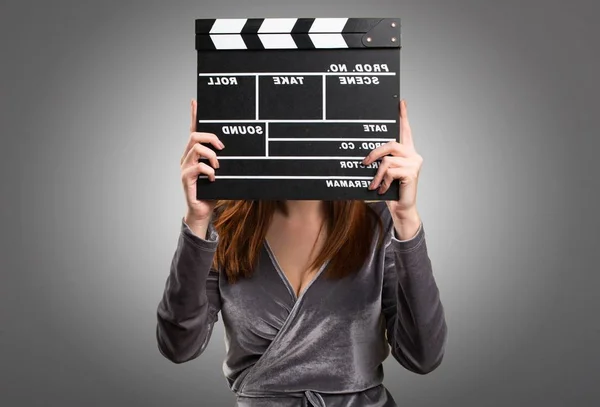 Beautiful young girl holding a clapperboard on textured background — Stock Photo, Image