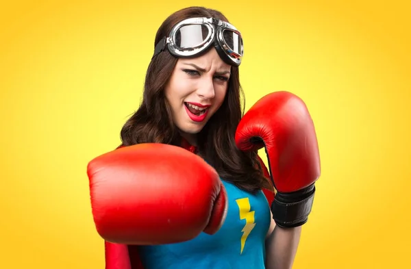 Hübsches Superheldenmädchen mit Boxhandschuhen auf buntem Hintergrund — Stockfoto