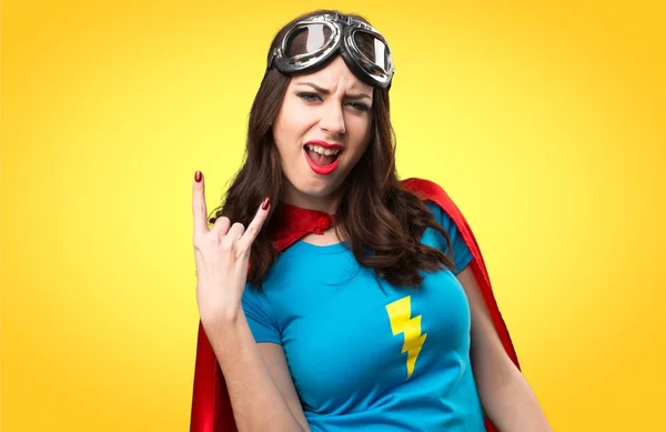Hezká superhrdina dívka dělat roh gesto na barevné pozadí — Stock fotografie