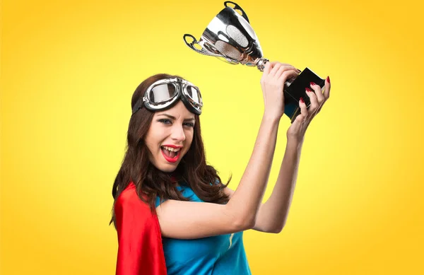 Pretty superhero girl holding a trophy on colorful background — Stock Photo, Image