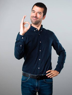 Yakışıklı adam gri arka plan üzerinde oturum Tamam yapma