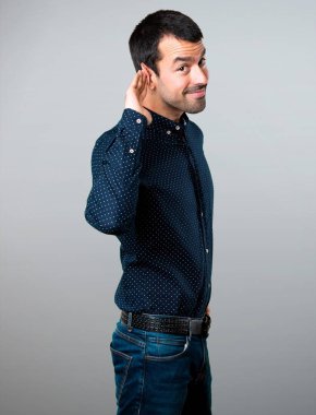 Yakışıklı adam gri arka plan üzerine bir şey dinleme