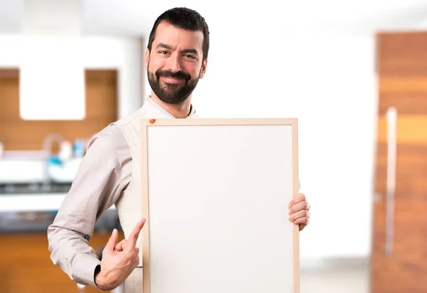 Bonito homem com colete segurando um cartaz vazio dentro da casa — Fotografia de Stock