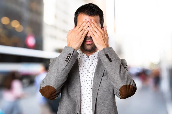 Schöner Mann, der seine Augen vor unkonzentriertem Hintergrund verdeckt — Stockfoto