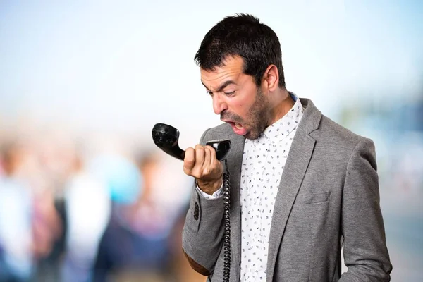 Frustrato bello uomo parlando con telefono vintage su sfondo sfocato — Foto Stock