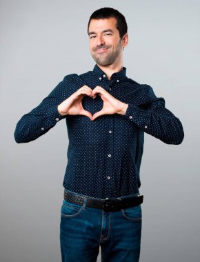 Yakışıklı adam gri arka plan üzerinde elleriyle bir kalp yapma