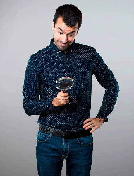 Handsome man with magnifying glass on grey background — Stock Photo, Image