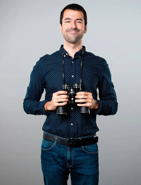 Pohledný muž s dalekohledem na šedém pozadí — Stock fotografie